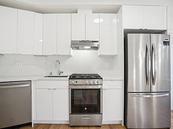 Kitchen with multiple cabinets, refrigerator, stove, range hood, and sink