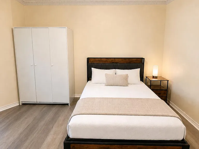 Spacious furnished bedroom with a full bed, bedside table with lamp, and a large wardrobe for ample storage.