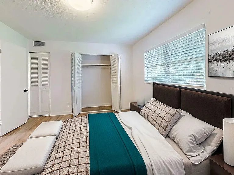 Inviting bedroom with a plush bed, modern decor, and a spacious closet, bathed in natural light from large windows.