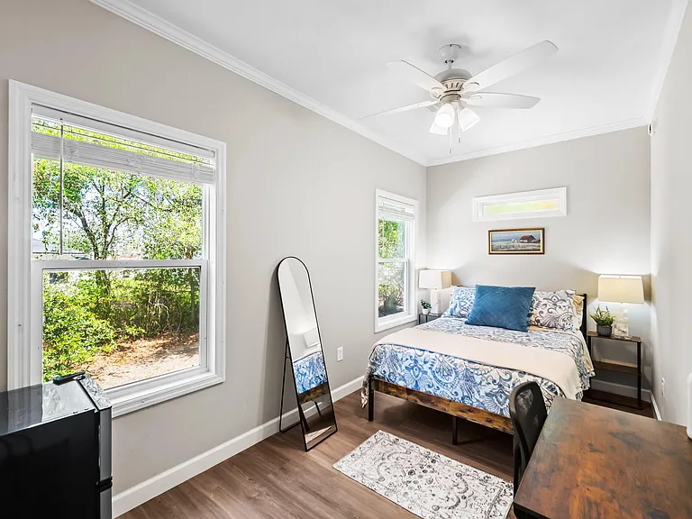 Furnished bedroom with large windows, ceiling fan, and a dedicated desk area for studying or working from home.
