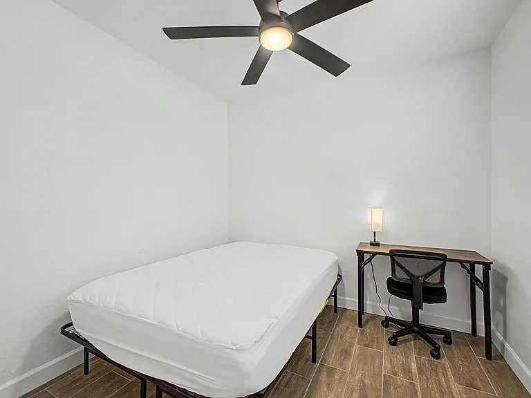 Private bedroom with ceiling fan, wood-look flooring, and a dedicated desk workspace beside the window.