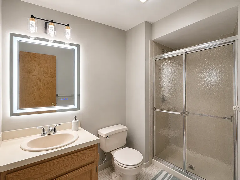Clean and comfortable primary bathroom with an LED mirror, modern lighting, and glass shower doors for a bright, fresh feel.