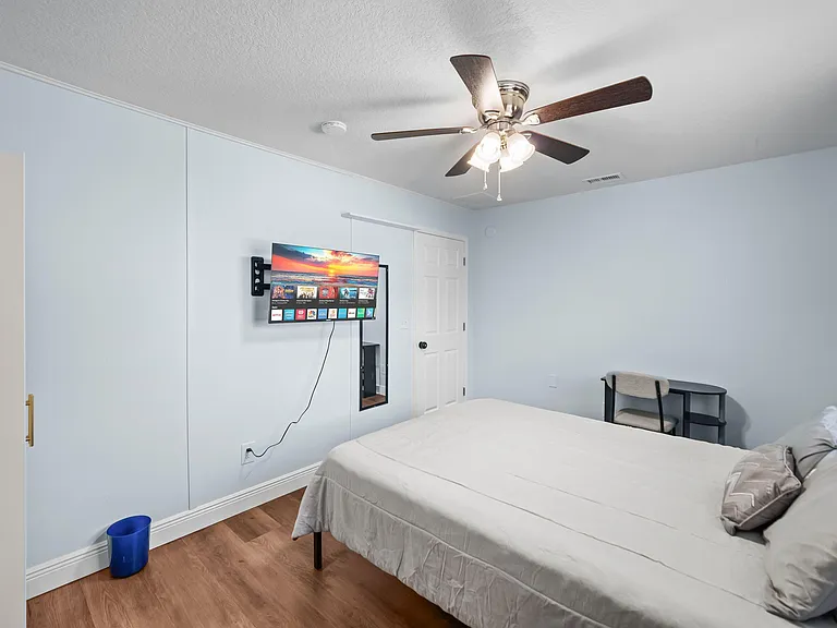 Private bedroom with ceiling fan, wall-mounted TV, and work desk, plus ample wall-to-wall closet storage.