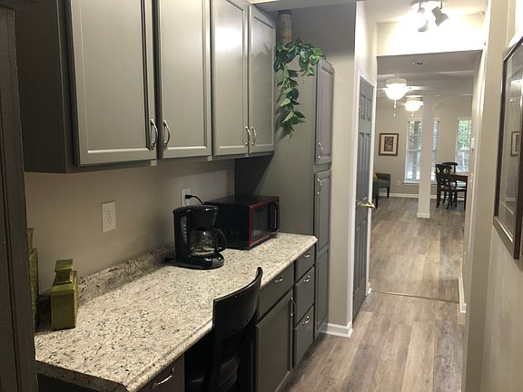 Photo taken outside full bathroom. Hallway features storage cabinets and desk area on left, and leads to kitchen (outside camera frame) on right .
