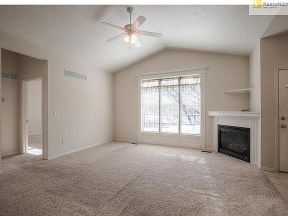 Carpeted living room with vaulted ceiling, ceiling fan, big sunny windows and gas fireplace.