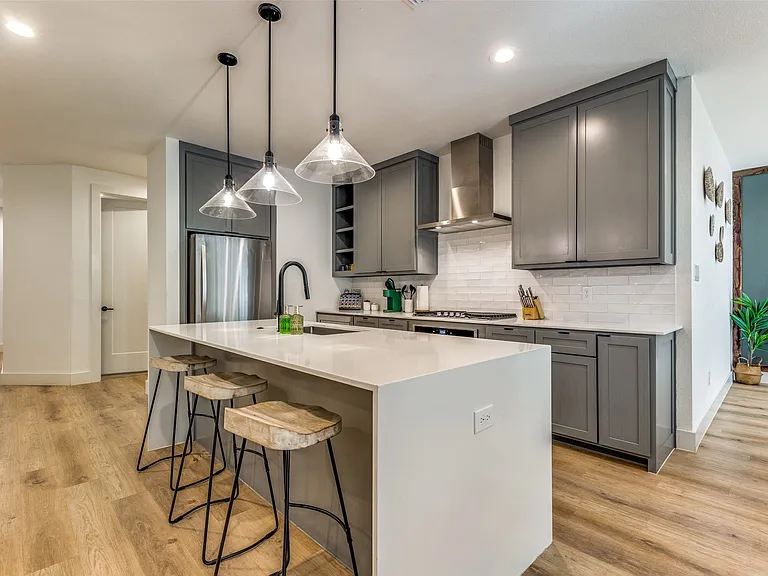 Modern kitchen featuring a large island with white countertop, gray cabinetry, stainless steel appliances, a subway tile backsplash, and wood-finish flooring