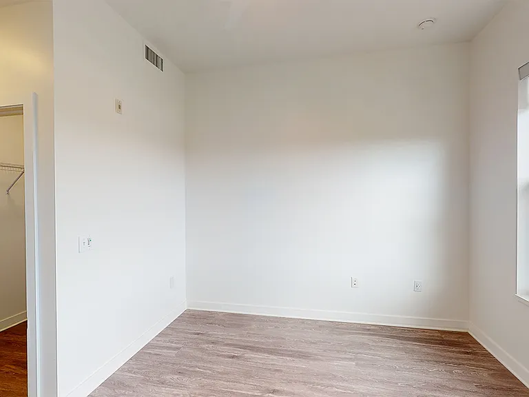 Spacious apartment bedroom with large closet and wood-style flooring.