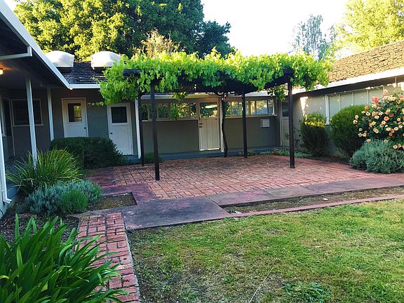 Brick patio with trellis and breezeway from garage to main house. (note that grass in this area has been replaced with artificial turf)