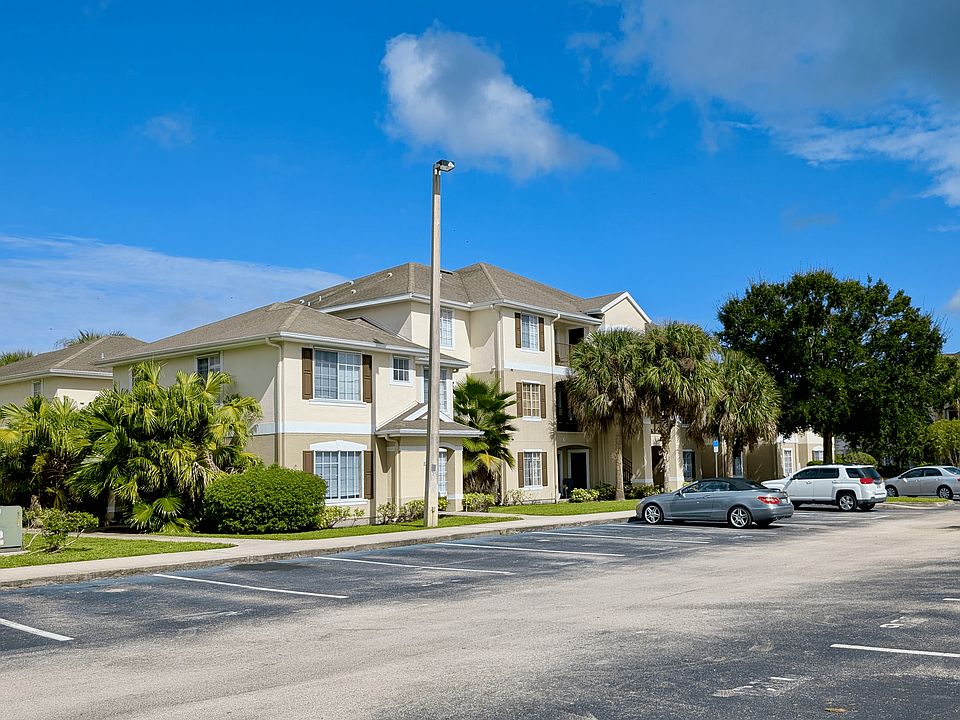 Charming apartment complex with lush palm trees, ample parking, and clear blue skies.