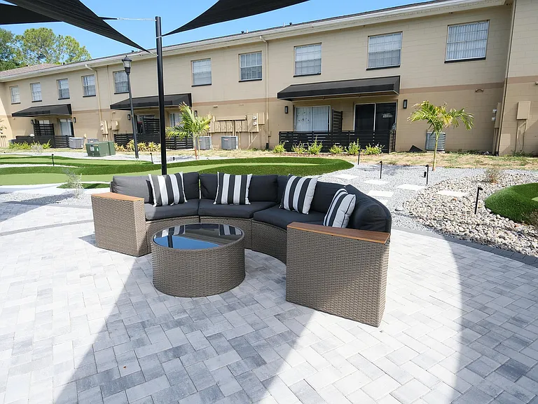 Chic outdoor patio featuring a stylish wicker sofa with striped cushions and a modern glass coffee table, set against charming townhouse exteriors.