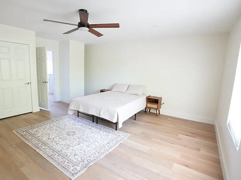 Spacious bedroom with wood-look floors, ceiling fan, large window, and closet, plus room for a desk or seating area.