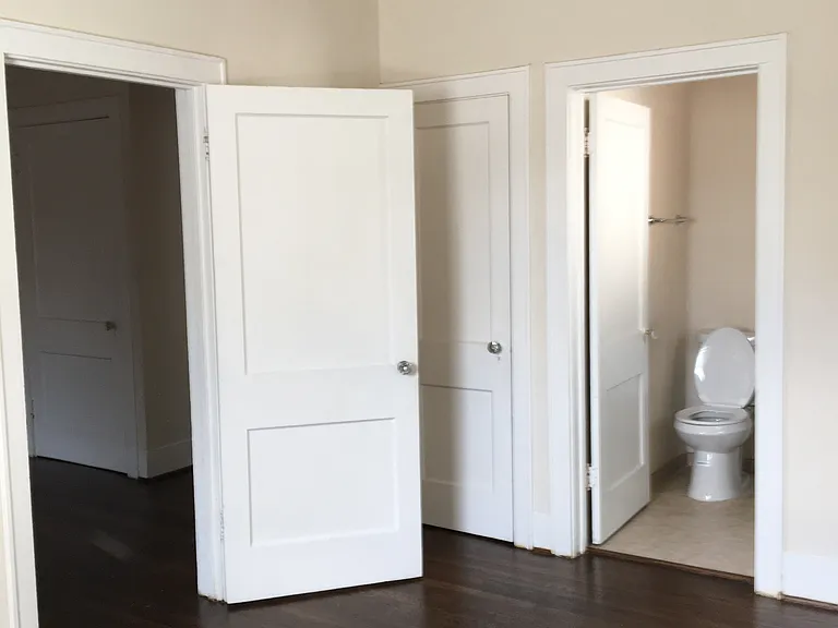 View from inside bedroom. Open door on left to living room. Closed door is a walking closet. Ceiling fan and split A/C unit.