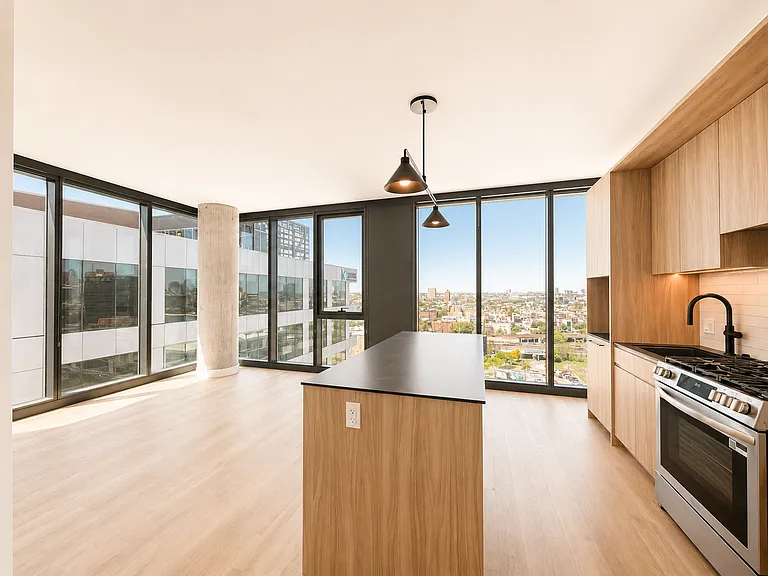 Sunlit 1-bed-plus-den home at Stead 220 in Fulton Market featuring an open kitchen with island and stainless steel gas range, light wood cabinetry, and wraparound corner windows with skyline views.