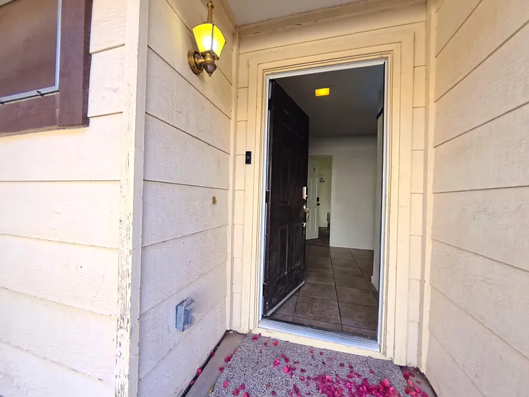 Covered front entry with exterior lighting and a defined threshold leading into a tiled foyer hallway.