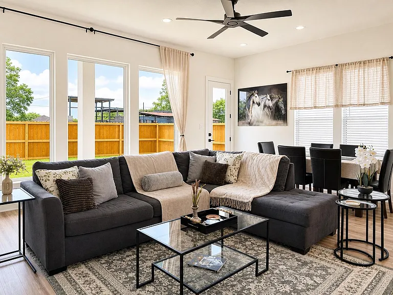 Open-concept living area with a large sectional, ceiling fan, and picture windows plus a dining nook near the patio door.