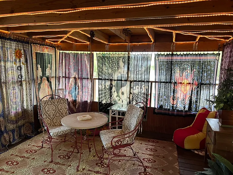 Lovely patio with table and chair seating, rope lighting, tapestry curtains, carpet, screened-in.