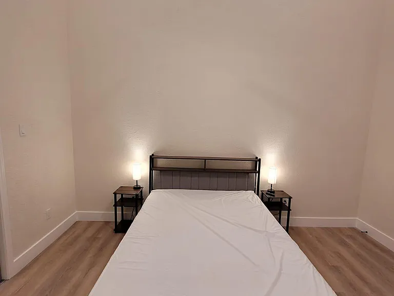 Simple bedroom with a bed frame, two nightstands with lamps, and a ceiling fan over easy-care flooring.