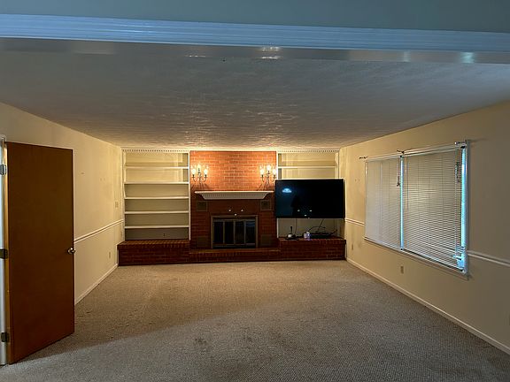 Large, open living room or den. Exposed brick fireplace (non functional) with large built-in shelves. Carpeted. Access the side porch.