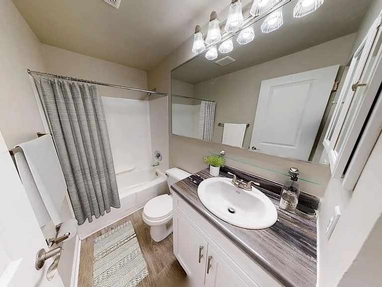 The Dickenson floor plan features a bright and updated bathroom with a large mirror, modern vanity, and wood-style flooring.