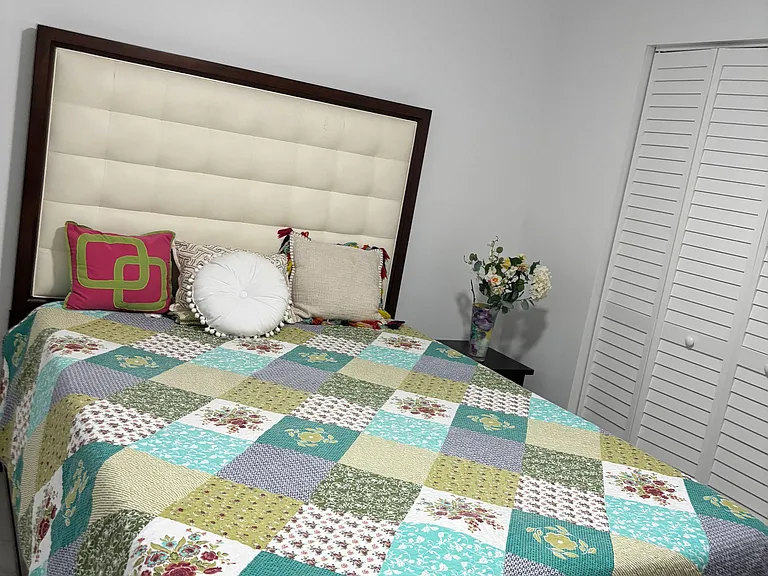 Furnished bedroom with a comfortable bed, padded headboard, ceiling fan, and a closet with louvered doors.