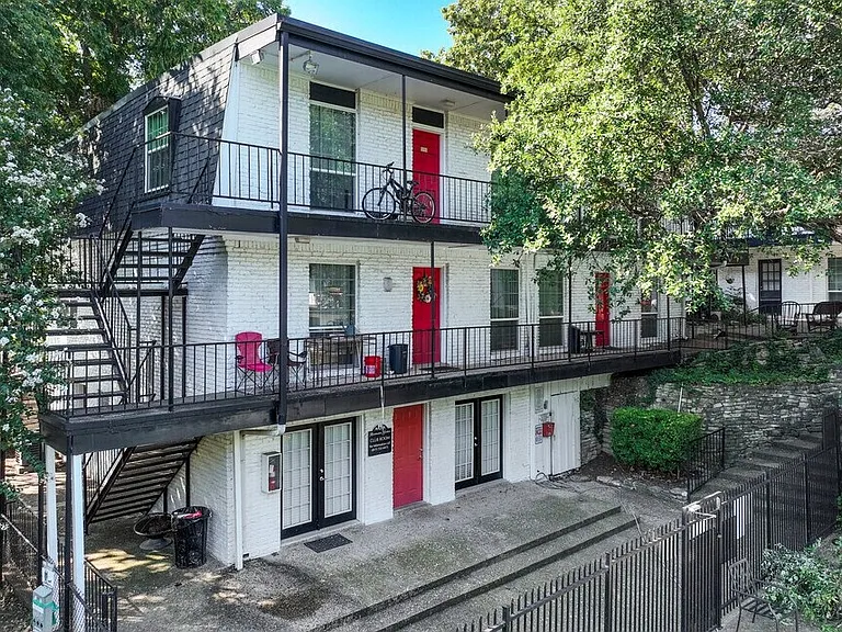 Charming two-story apartment building with modern black railings, vibrant red doors, and lush greenery_offering a welcoming and stylish first impression.