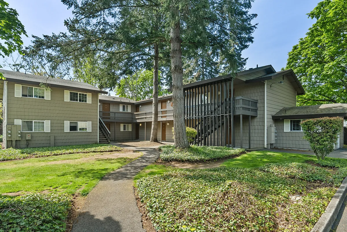 Picturesque view of a two-story apartment building surrounded by lush greenery. - Maple Grove Apartments