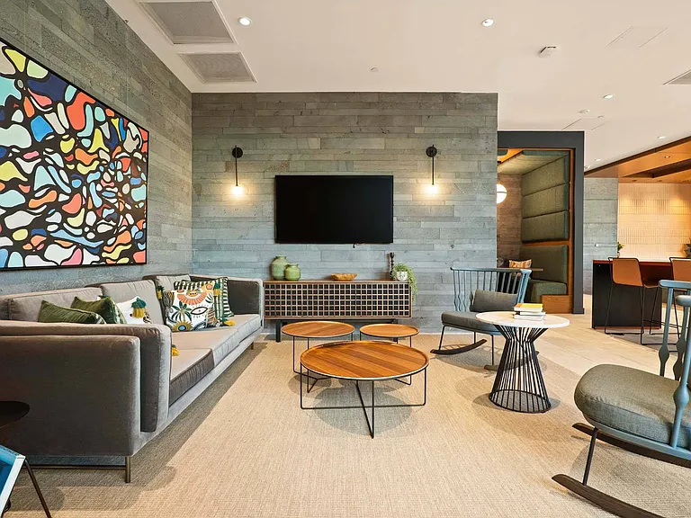 Step into a modern lounge featuring a sleek grey couch, a wooden coffee table, and a striking abstract painting.