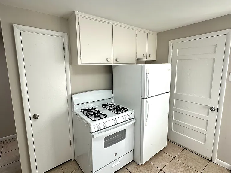 Charming kitchen with classic white appliances, ample cabinet storage, and modern tiled flooring.