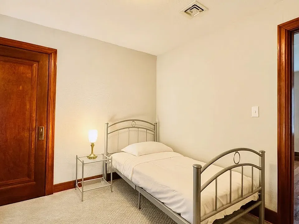 Cozy bedroom with a large glass window overlooking the driveway, bringing in natural light and fresh air. Includes a convenient walk-in closet. Carpeted flooring helps maintain warmth and comfort during winter months. Ideal for a peaceful retreat.
