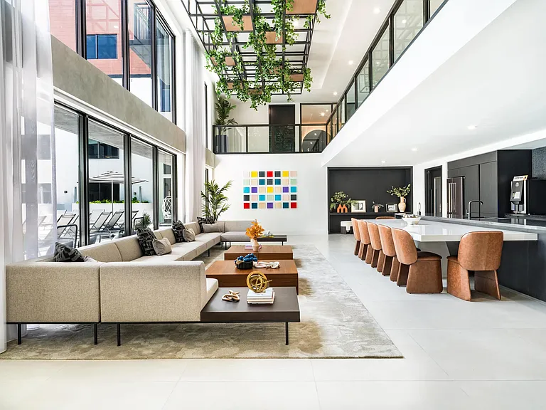 Poolside clubroom with communal seating, a demonstration kitchen, and suspended greenery creating an inviting break from the Coral Springs sun.