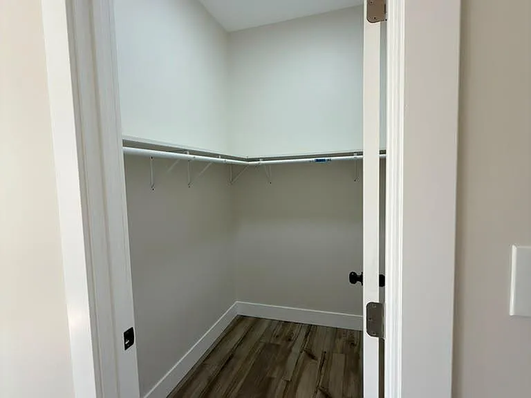 Walk-in closet with wraparound hanging rods, overhead lighting, and durable wood-look flooring for easy organization.