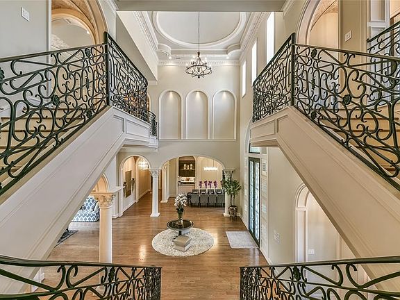 The main staircase off the grand foyer highlights the two story ceilings adorned with layers of crown molding and recessed art niches. The intricate custom railing splits to access two wings of the residence.