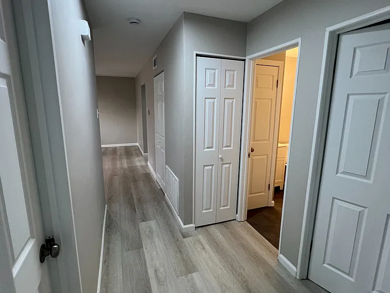 End of hallway view from back-hall bedroom showing 2 other rooms on either side of hallway along with entry to full bath with neighboring utility closet.