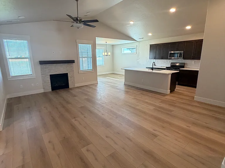 The spacious open-concept living area features a beautiful fireplace as its focal point, creating a warm and inviting atmosphere. Gorgeous wood flooring flows throughout the space, seamlessly connecting the living, dining, and kitchen areas.