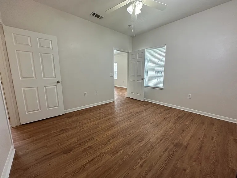 Bright and inviting bedroom with elegant wood-style floors, ceiling fan, and ample natural light from large window. Bright and inviting bedroom with elegant wood-style floors, ceiling fan, and ample natural light from large window.