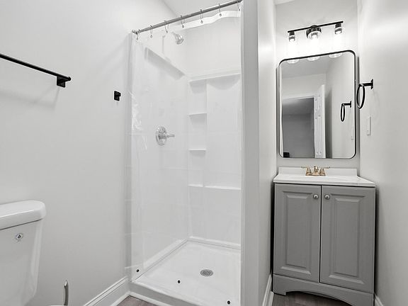 Full bathroom featuring a walk-in shower with built-in shelving, a vanity with storage, and an updated lighted mirror.