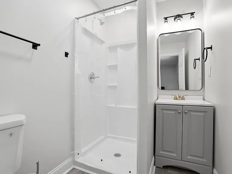 Full bathroom featuring a walk-in shower with built-in shelving, a vanity with storage, and an updated lighted mirror.