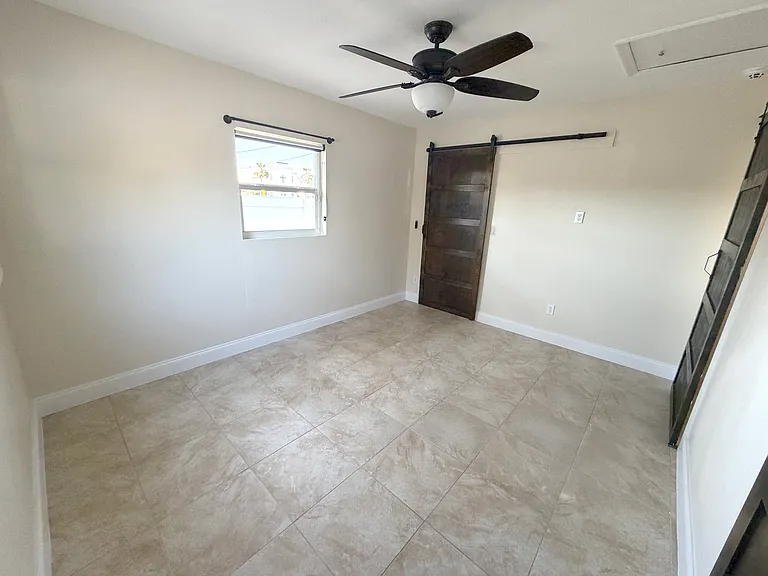 The master bedroom offers abundant natural light, a ceiling fan for comfort, and modern barn doors. (Angle 3)