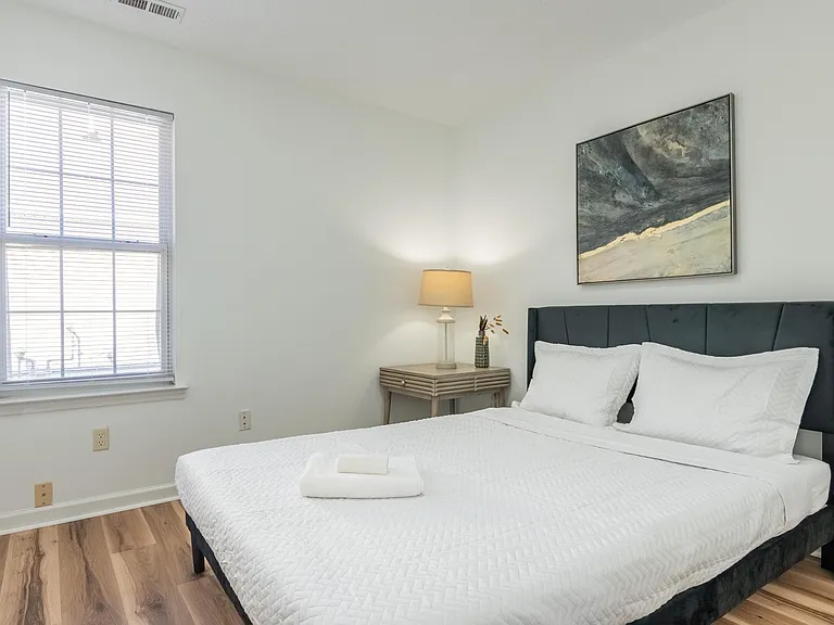 Spacious bedroom with a large window, comfortable bed, and a nightstand with lampideal for restful nights and easy morning r
