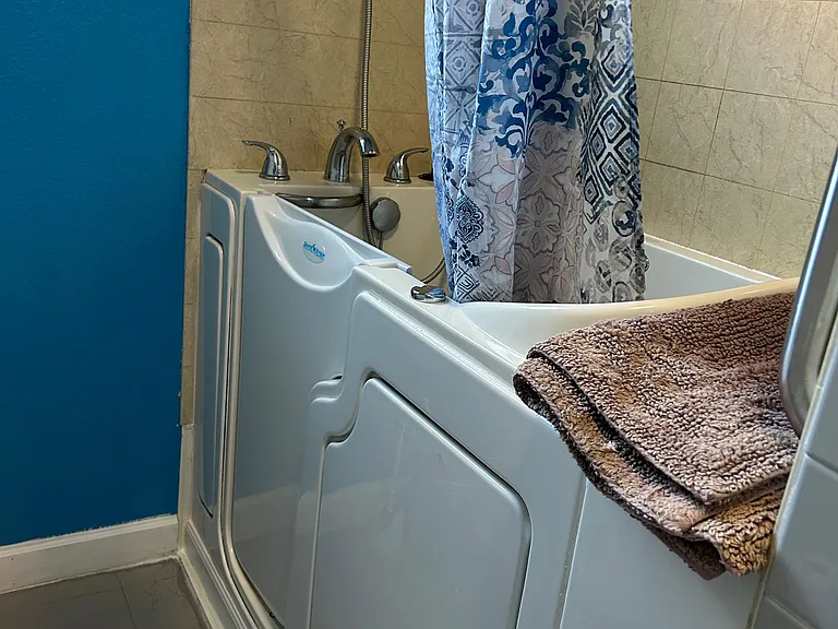 Full tub/shower combo with tiled surround, handheld showerhead, and a window for ventilation and natural light.