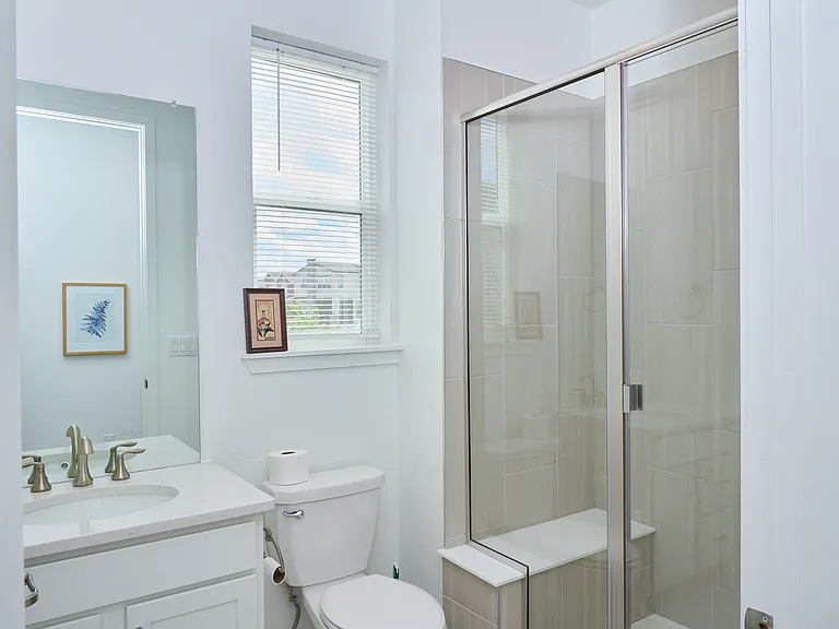 Bathroom with vanity sink, toilet, and shower. Tile flooring throughout. Large mirror.