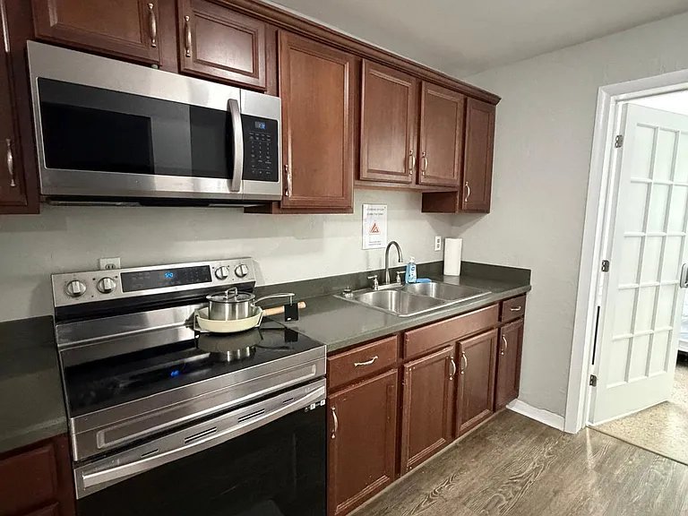 Efficient galley kitchen with ample wood cabinetry, stainless-steel range and microwave, and a double-basin sink.
