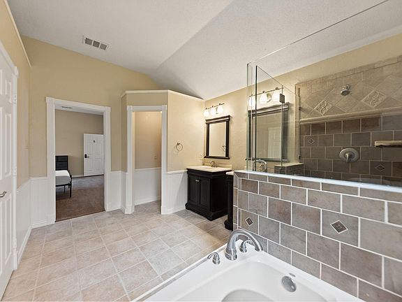 Spacious bath with double-sink vanity, framed mirrors, and a tiled walk-in shower with glass partition.