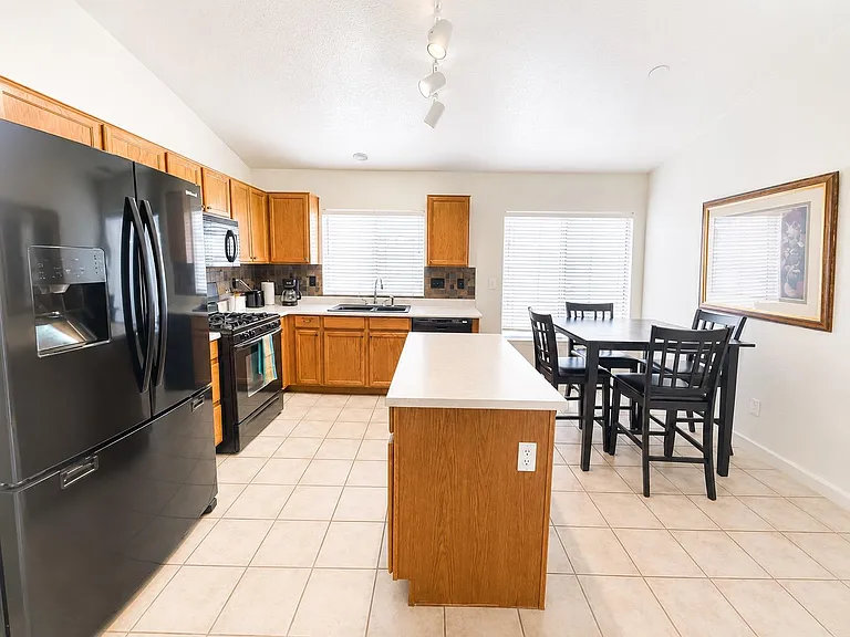 Open kitchen with center island, ample cabinetry, full appliance suite, and adjacent dining area with large windows.