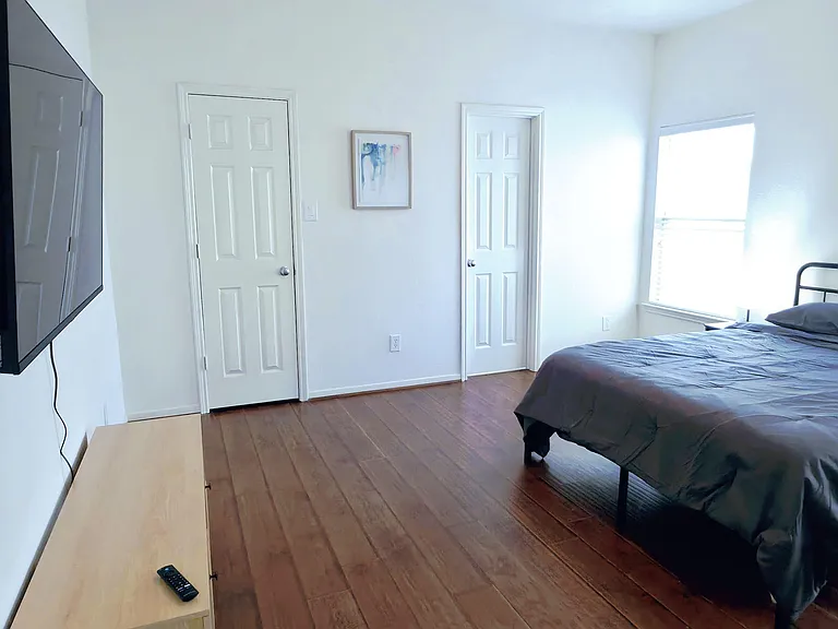 Spacious bedroom with wood-look flooring, ceiling fan, large window, and wall-mounted TV with a dedicated closet.