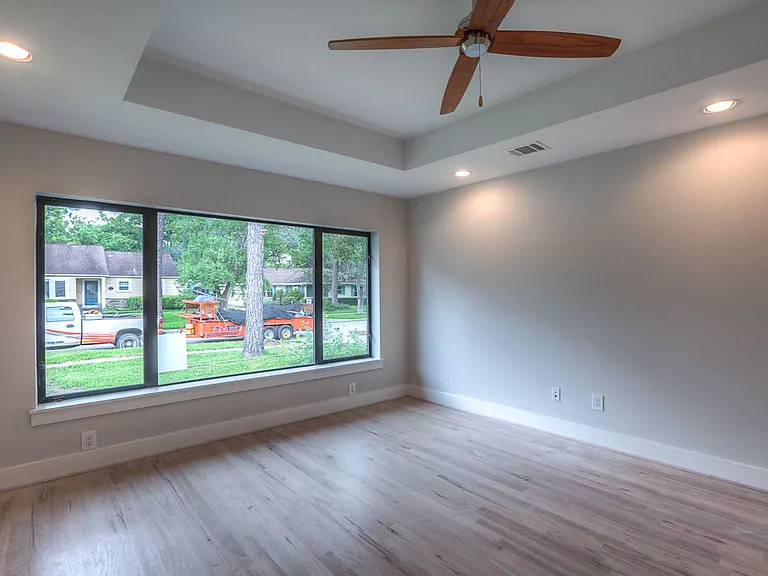 Spacious study/bedroom with tray ceiling, ceiling fan, oversized picture window, and refinished hardwood floors
