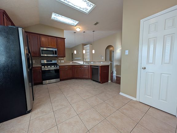 This bright kitchen features warm cabinetry, stainless steel appliances_including the refrigerator!_and a sleek tile floor. Modern pendant lights over the breakfast bar illuminate the open view into the living area, making it ideal for entertaining.