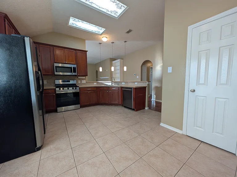 This bright kitchen features warm cabinetry, stainless steel appliances_including the refrigerator!_and a sleek tile floor. Modern pendant lights over the breakfast bar illuminate the open view into the living area, making it ideal for entertaining.