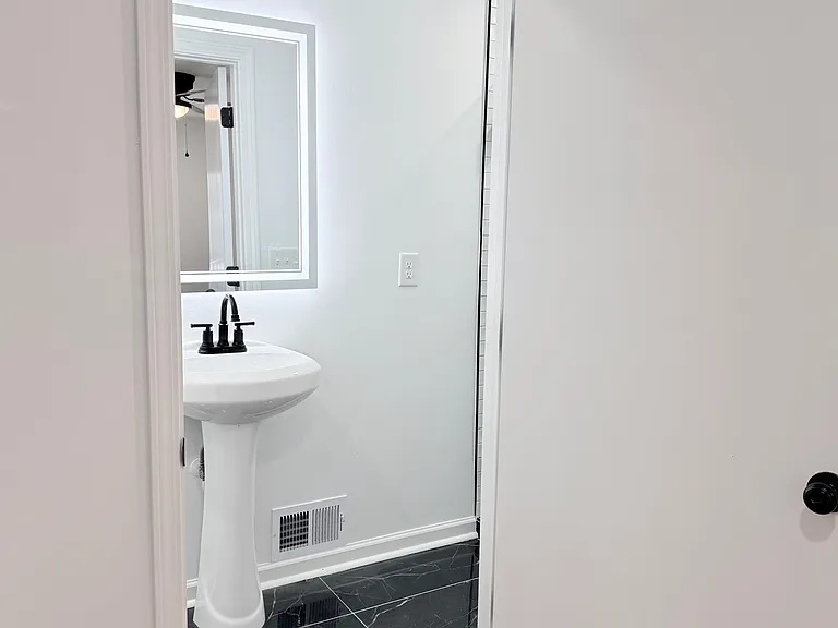 Bathroom features a pedestal sink with framed mirror, matte-black fixtures, and tile flooring for easy cleaning.
