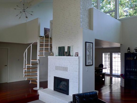 View from sunken living room showing spiral stair to loft. Bedrooms are off of hall to the left. All bedrooms and living spaces are on main. Double-sided fireplace is NOT operational. French doors are to back deck.
